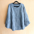 The Happy Shoe Shop Cinnamon Creations blue chunky knit oversized poncho with cable texture on a black hanger.