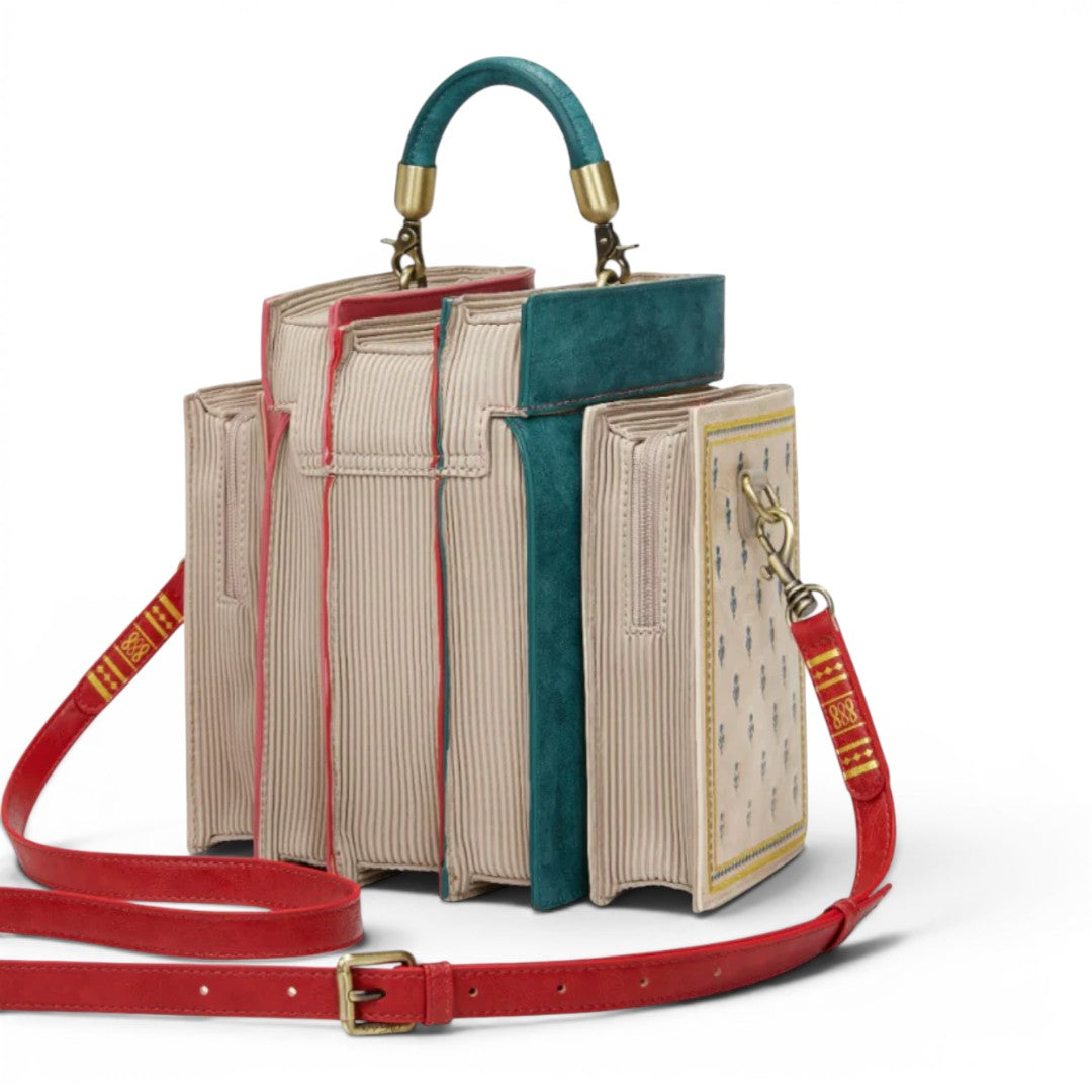 The Happy Shoe Shop Bookshelf Boulevard Book Stack Box Bag is a vegan leather handbag designed to look like a stack of books in cream, teal, and red with gold hardware.