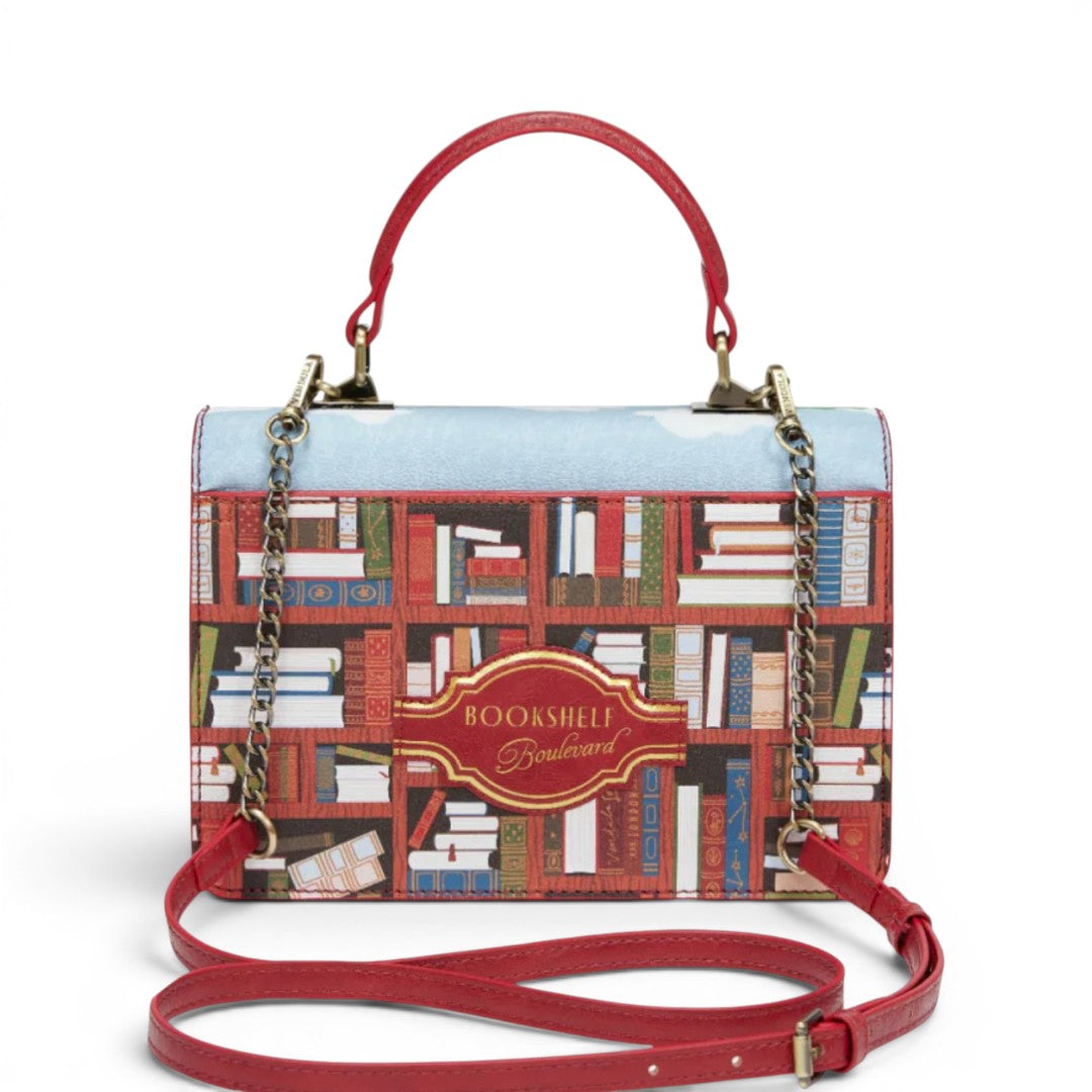 The Happy Shoe Shop Bookshelf Boulevard Cassie Bag with red handles and strap, featuring a bookshelf print and book-shaped closure.
