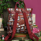 The Happy Shoe Shop Bookshelf Boulevard Tessa Backpack features a bookshelf print, vegan leather trim, and adjustable straps. It has a top handle and multiple pockets.