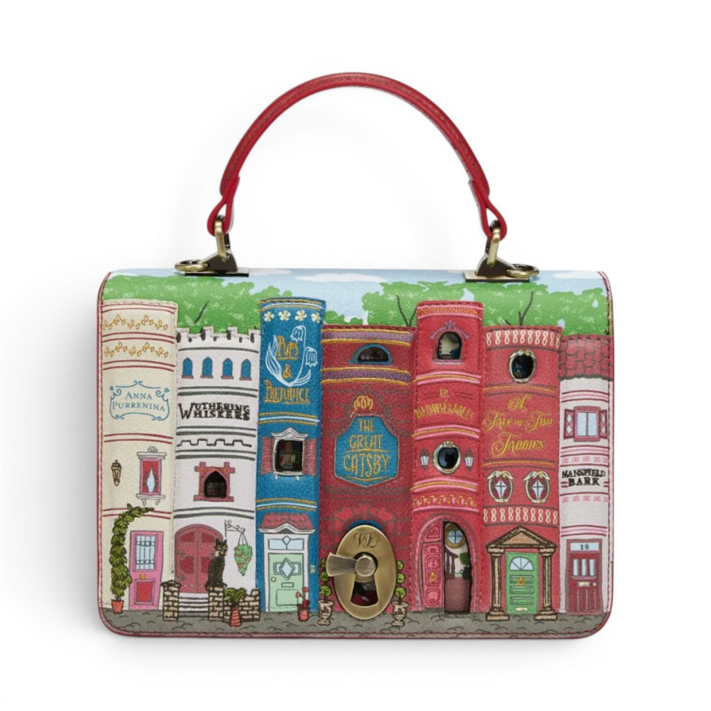 The Happy Shoe Shop Bookshelf Boulevard Cassie Bag, a vegan leather handbag with a book-shaped turn-lock closure and detailed cityscape artwork.