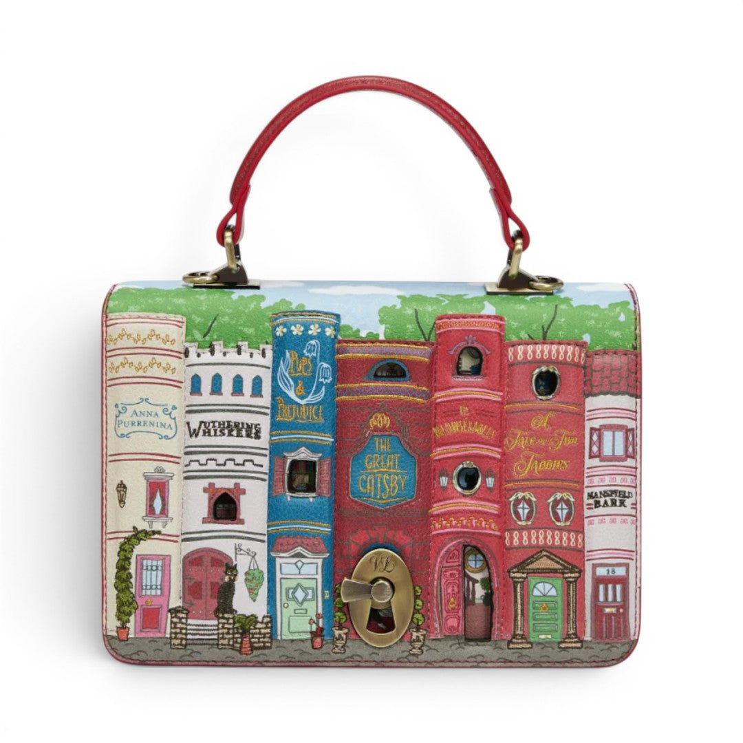 The Happy Shoe Shop Bookshelf Boulevard Cassie Bag, a vegan leather handbag with a book-shaped turn-lock closure and detailed cityscape artwork.