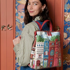 The Happy Shoe Shop Bookshelf Boulevard Tessa Backpack features a whimsical book spine design with "Wuthering Whiskers" and "The Great Gatsby" details. Vegan leather.