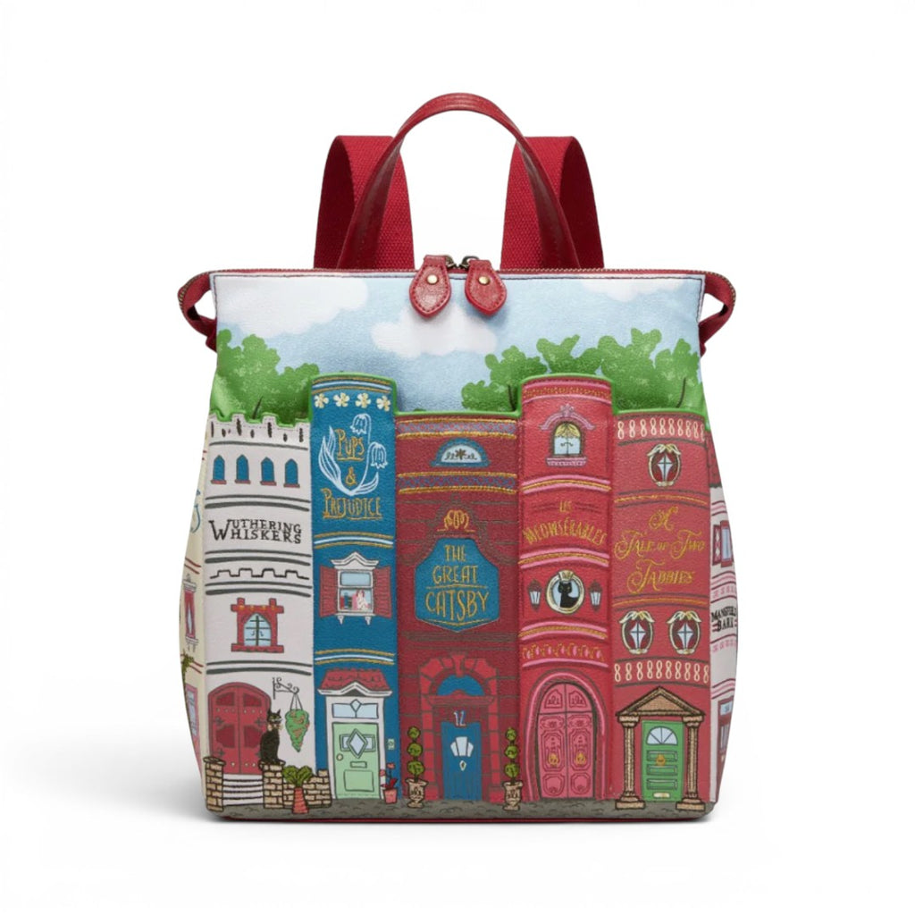 The Happy Shoe Shop Bookshelf Boulevard Tessa Backpack, a vegan leather backpack with a whimsical book spine design, red straps, and a sky background.