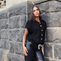 Model wearing a black Cinnamon Creations sleeveless knit crop top with button front and drawstring hem by The Happy Shoe Shop