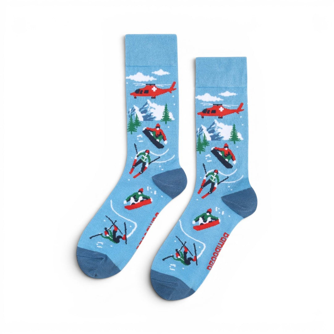 The Happy Shoe Shop Men's Snow Escape bamboo socks in sky blue with skiers, snowboarders, helicopters, and mountains.