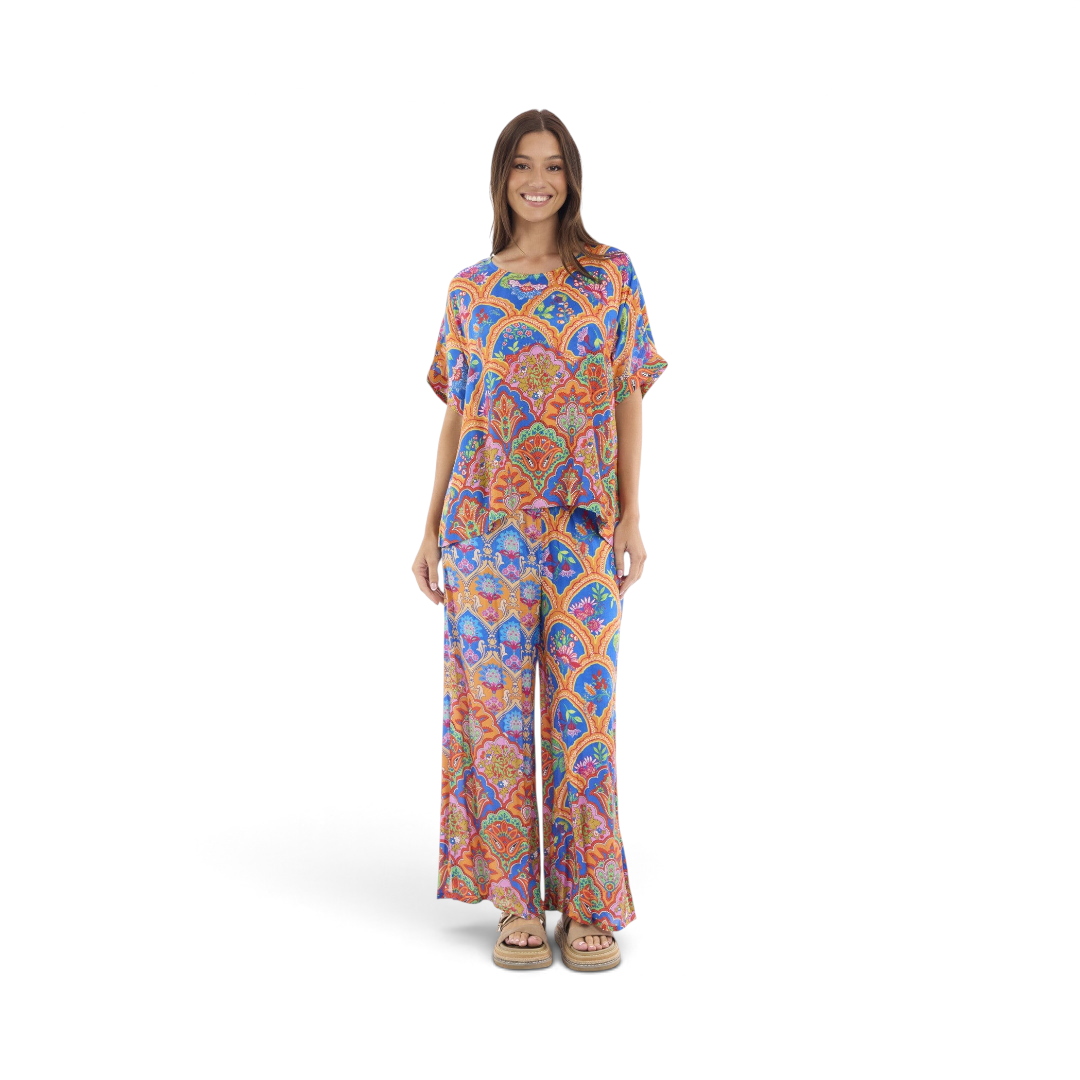 Model wearing The Happy Shoe Shop Orientique Escape Aurora wide-leg rayon pants with a vibrant artistic paisley print.