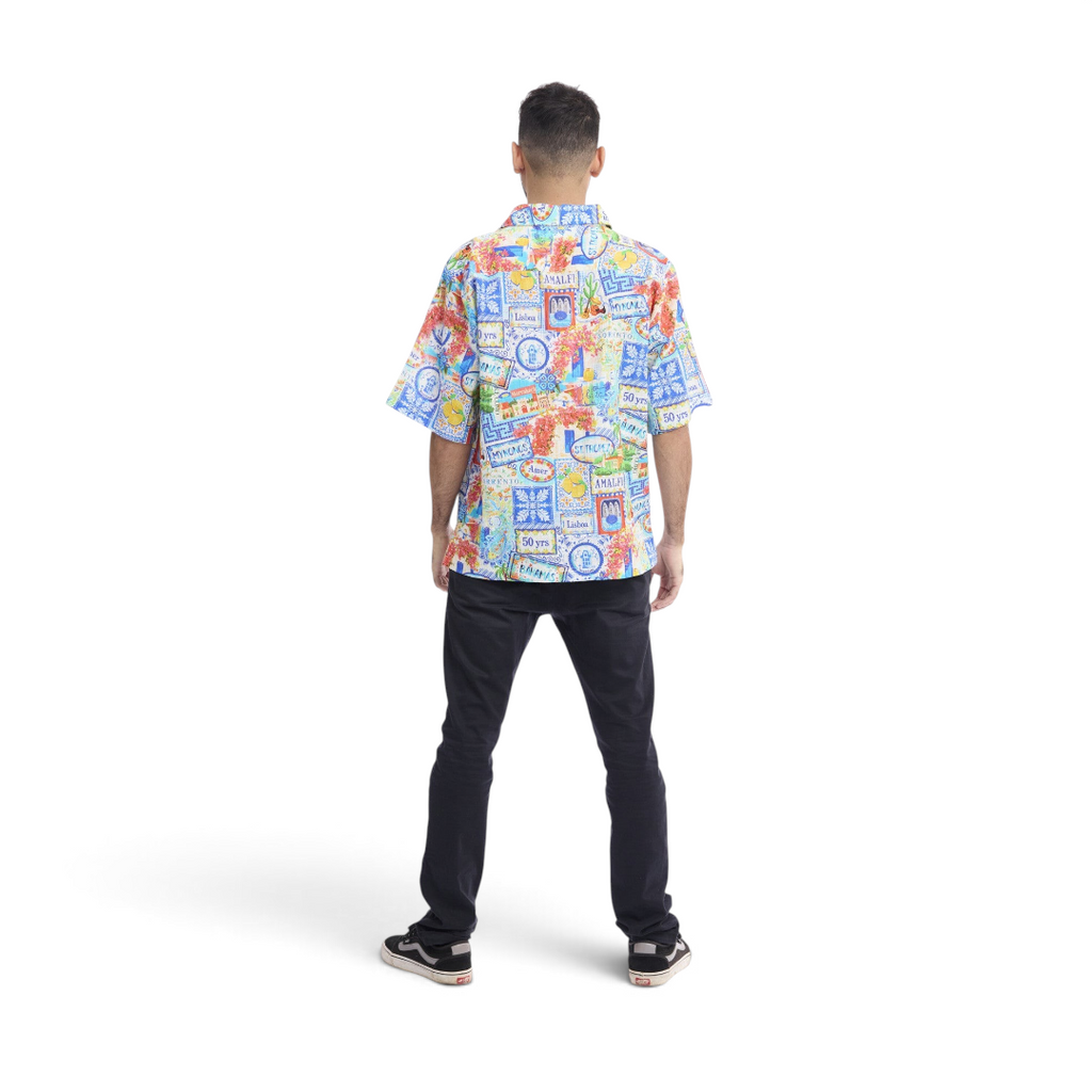 Back view of a man wearing a The Happy Shoe Shop Orientique short sleeve shirt with a colourful travel-themed print.