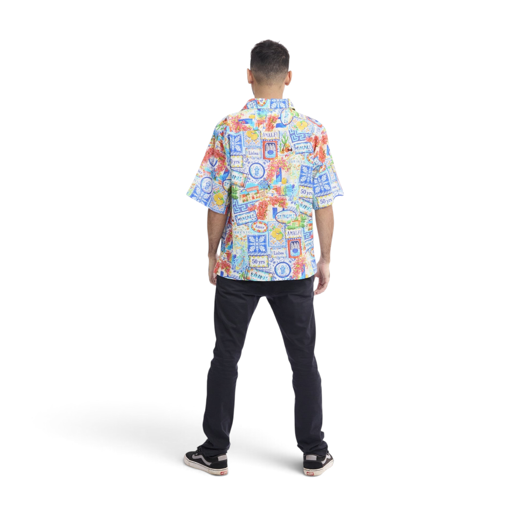 Back view of a man wearing a The Happy Shoe Shop Orientique short sleeve shirt with a colourful travel-themed print.