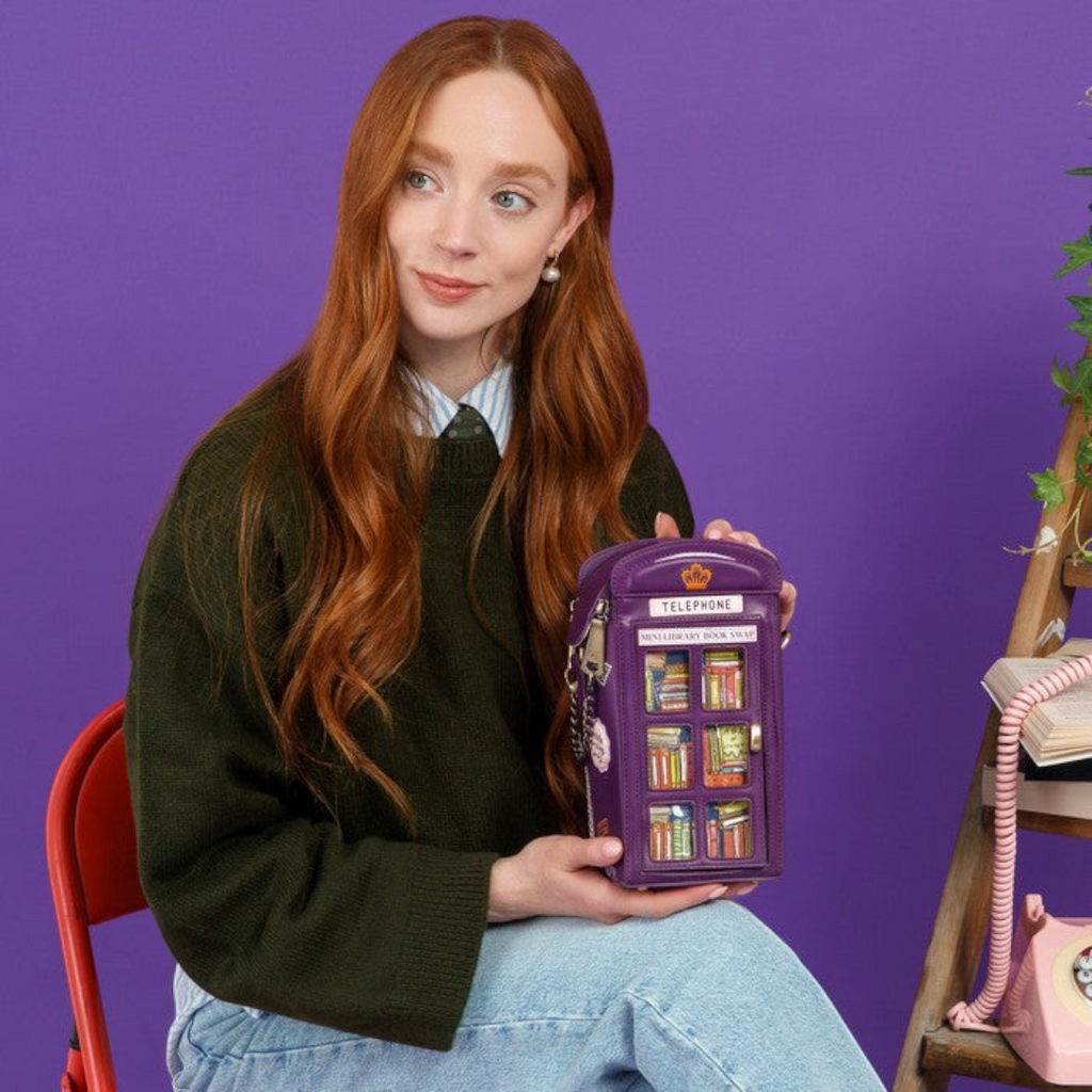 The Happy Shoe Shop Vendula London purple telephone box novelty bag held by a woman against a purple background.