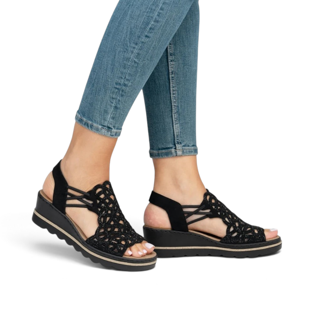 The Happy Shoe Shop Rieker black wedge sandals with intricate cut-out textile upper and cushioned insole on a model