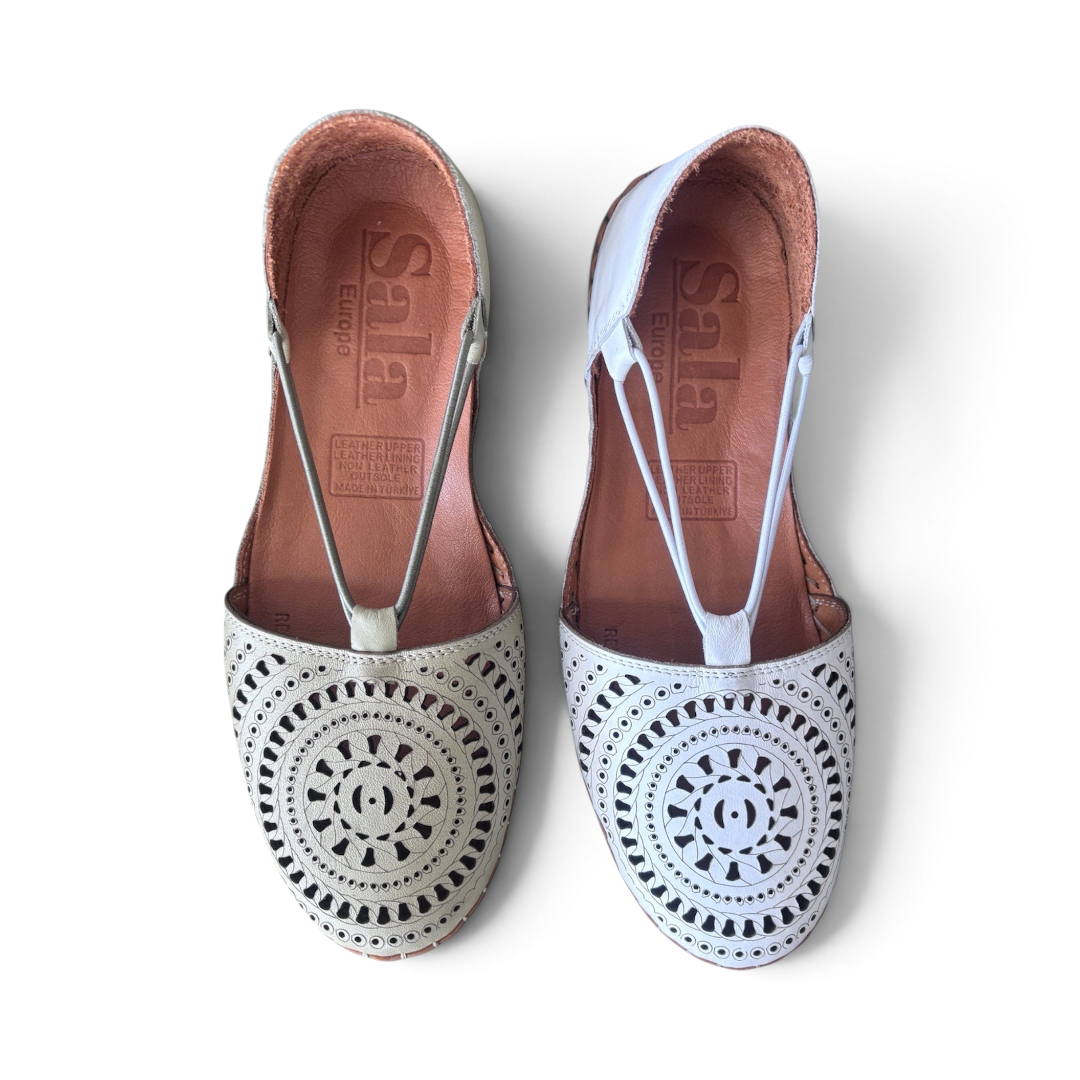 The Happy Shoe Shop Sala Reed flats featuring white and cream laser-cut leather uppers with a T-strap design.