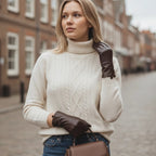The Happy Shoe Shop Thomas Cook women's chocolate brown leather gloves worn by a blonde woman in a cream sweater.