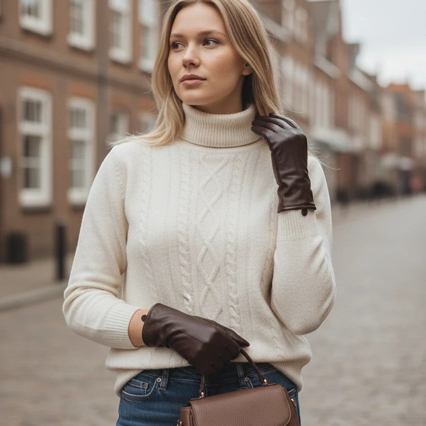 The Happy Shoe Shop Thomas Cook women's chocolate brown leather gloves worn by a blonde woman in a cream sweater.