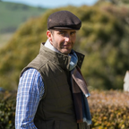 Thomas Cook Samuel Driver Cap in dark brown wool with a subtle embossed logo trim. Worn by a man outdoors.