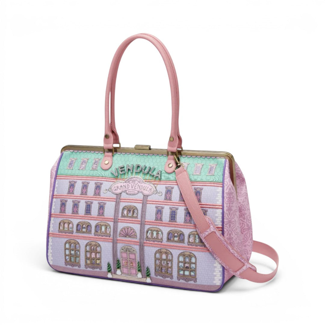 The Happy Shoe Shop Grand Vendula Hotel Sylvie Clip Frame Holdall Bag with pink handles and strap, featuring a hotel facade print.